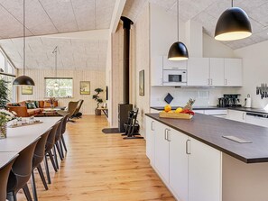 Eine moderne Küche mit weißen Schränken, einer Holzauskleidung und einem Essbereich mit einem langen Tisch und Stühlen.