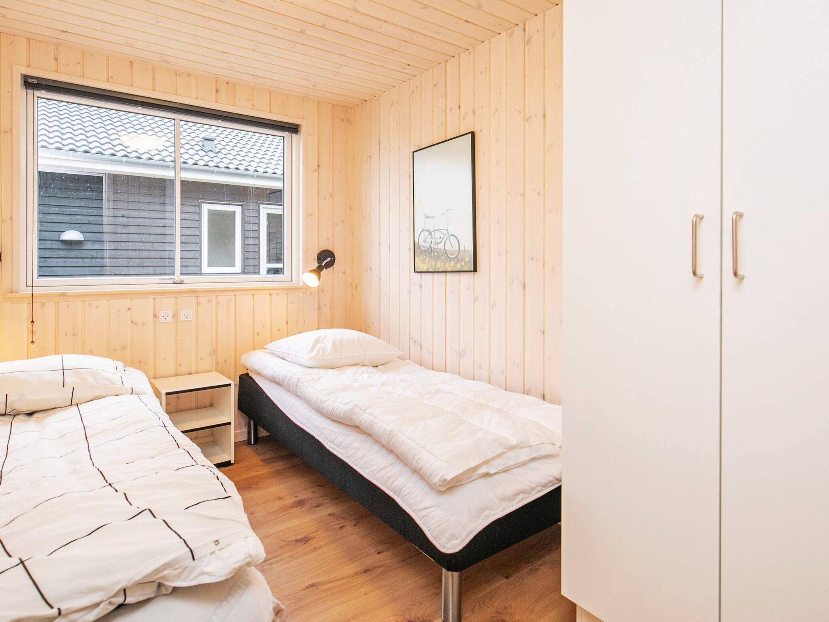 A room with two beds, a window, a wall-mounted lamp, and a wardrobe.