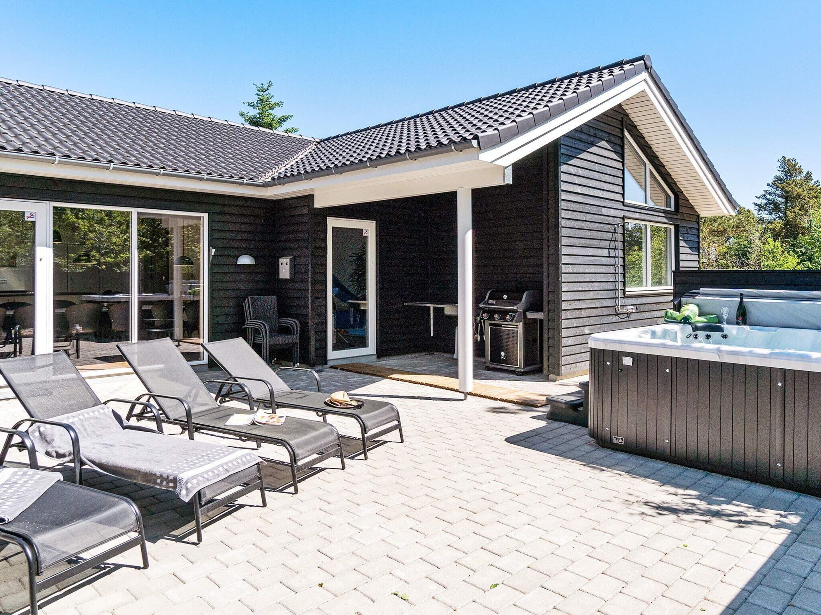 A modern house with a patio area featuring lounge chairs and a hot tub.