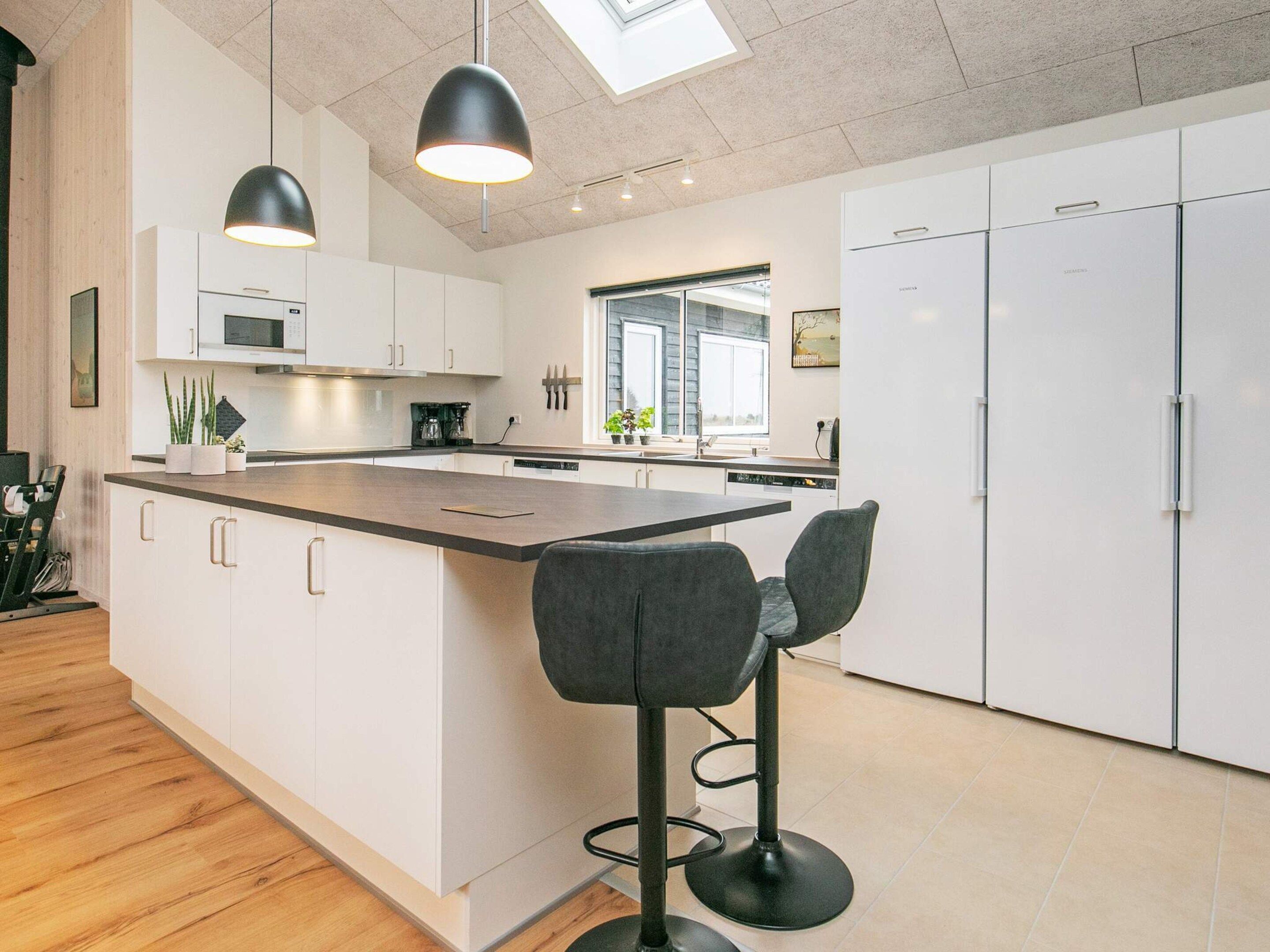 Et moderne køkken med en central ø, barstole og et ovenlysvindue.