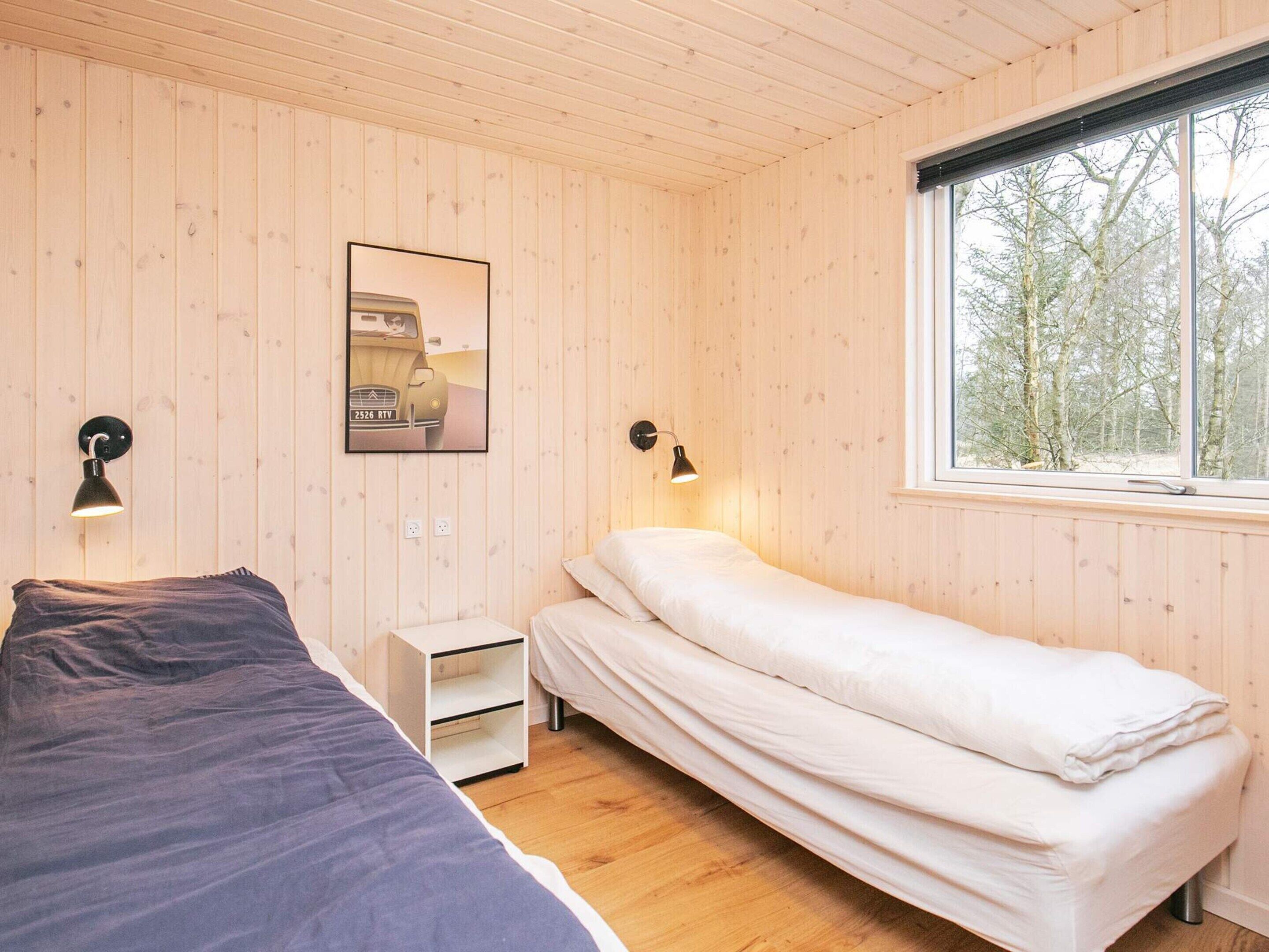 A room with two beds, a window with a view of trees, and a wall-mounted picture.