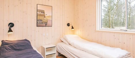 A room with two beds, a window with a view of trees, and a wall-mounted picture.