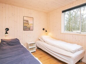 A room with two beds, a window with a view of trees, and a wall-mounted picture.