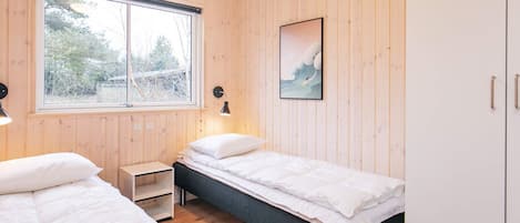 A room with two beds, a window, a wall-mounted lamp, and a framed picture.