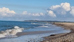 A beach with waves, pebbles, and a distant person.