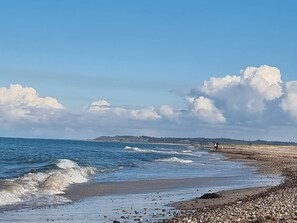 A beach with waves, pebbles, and a distant person.