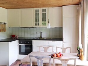 A kitchen with white cabinets, a black countertop, a sink, and a dining table with chairs. There are wooden utensils hanging on the wall and a bowl of fruit on the table. - 4 Person Holiday Home in Asljunga (Asljunga)