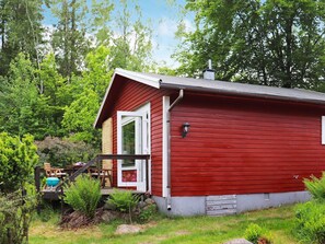 A red wooden cabin with a porch, surrounded by greenery. - 4 Person Holiday Home in Asljunga (Asljunga)