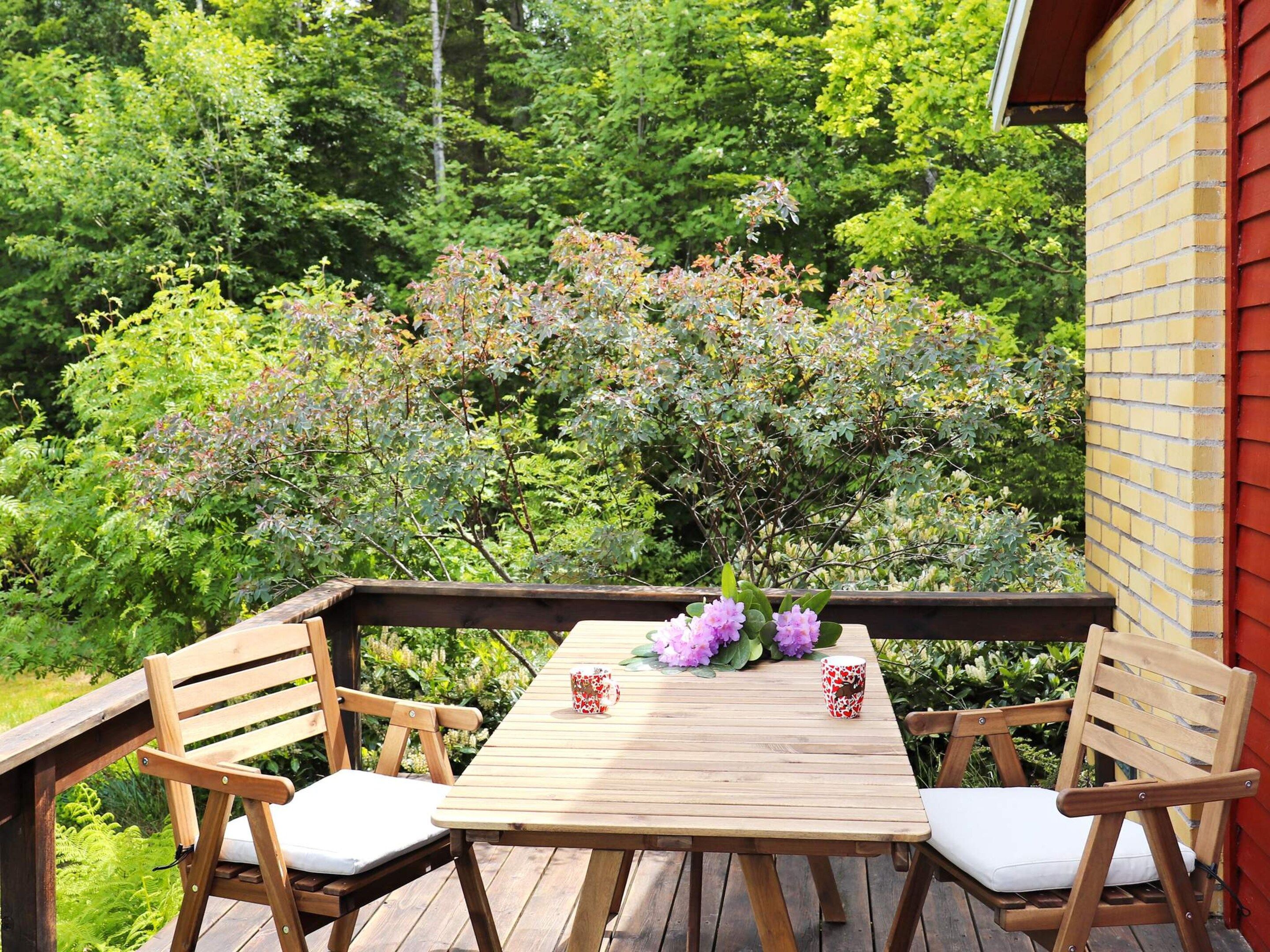 A wooden deck with two chairs and a table, surrounded by lush greenery and trees.