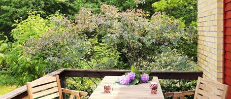 A wooden deck with two chairs and a table, surrounded by lush greenery and trees.