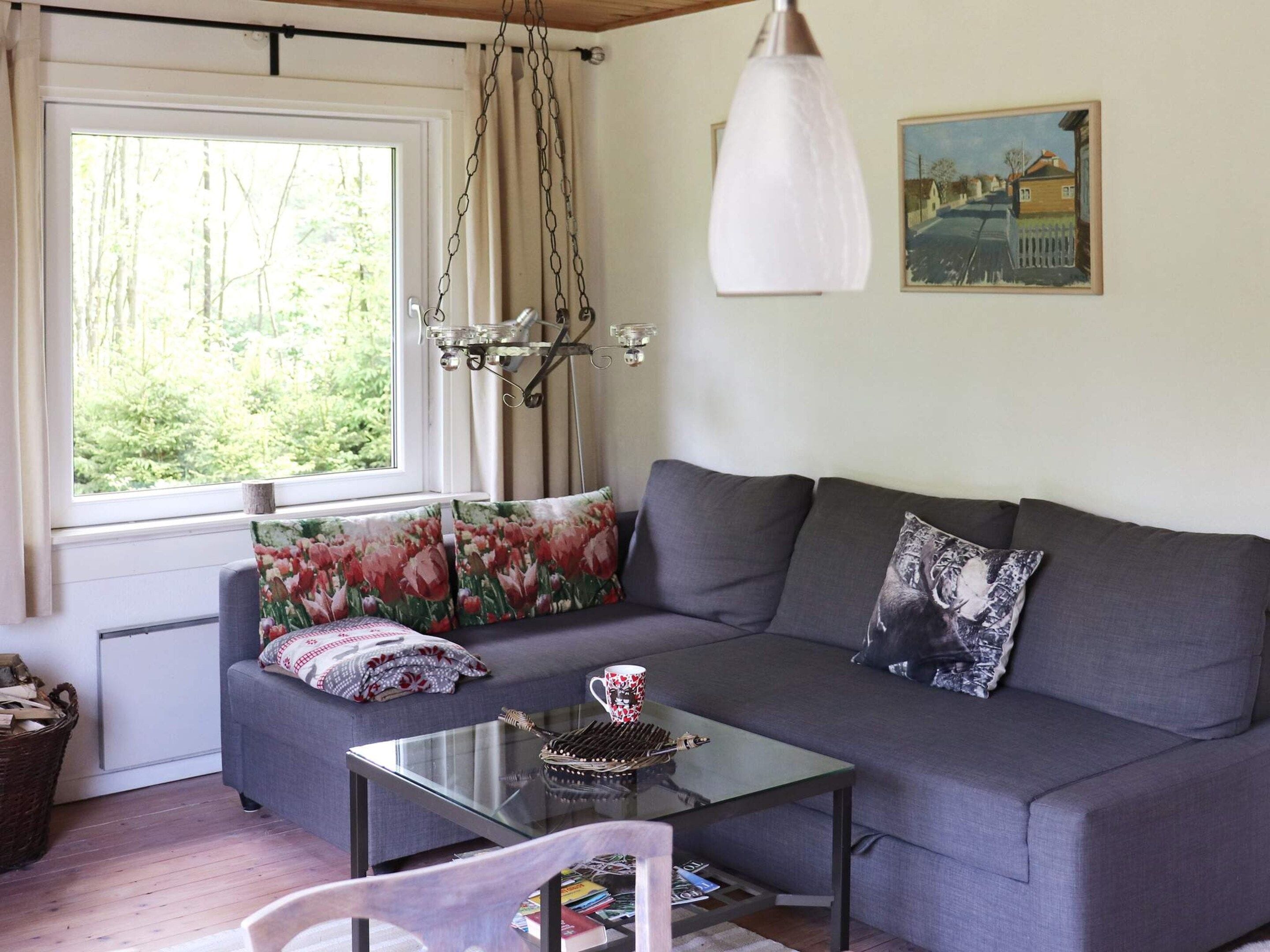 Un salón acogedor con un sofá gris, una mesa de centro de vidrio y una ventana con cortinas.