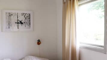 Un dormitorio con cama, lámpara de pared, ventana con cortinas e imagen en el marco colgada en la pared.