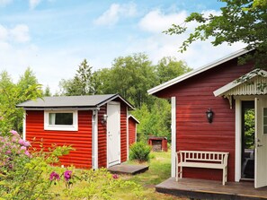 Deux cabanes rouges aux bordures blanches, un banc en bois et un jardin parsemé de fleurs violettes.
