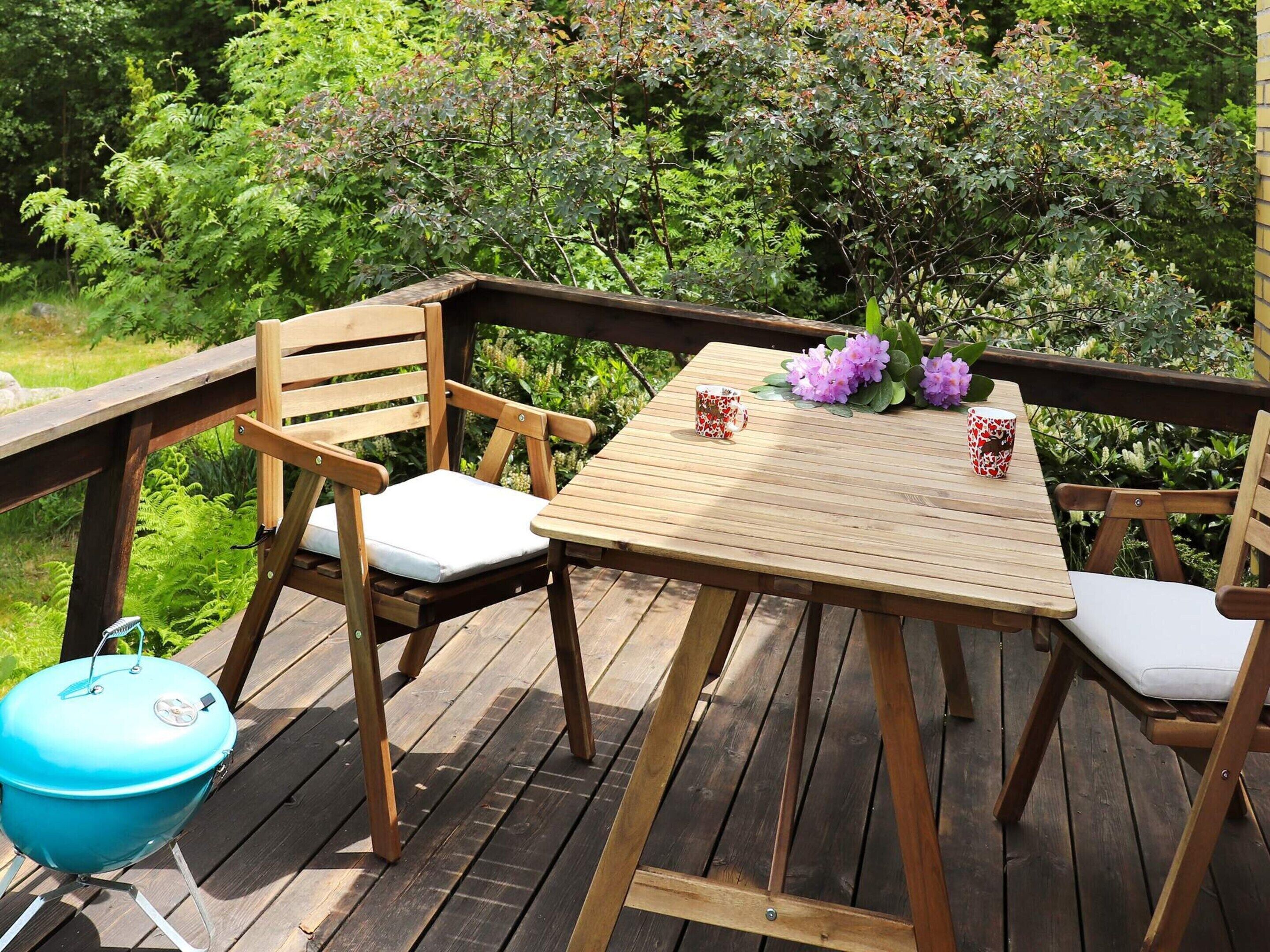 A wooden deck with a table and chairs, a grill, and a flower arrangement.