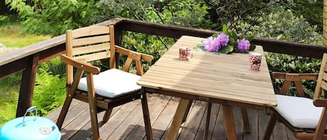 A wooden deck with a table and chairs, a grill, and potted plants.