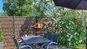 An outdoor patio with a table and chairs, a guitar leaning against a bamboo fence, and a bird sculpture on the ground.