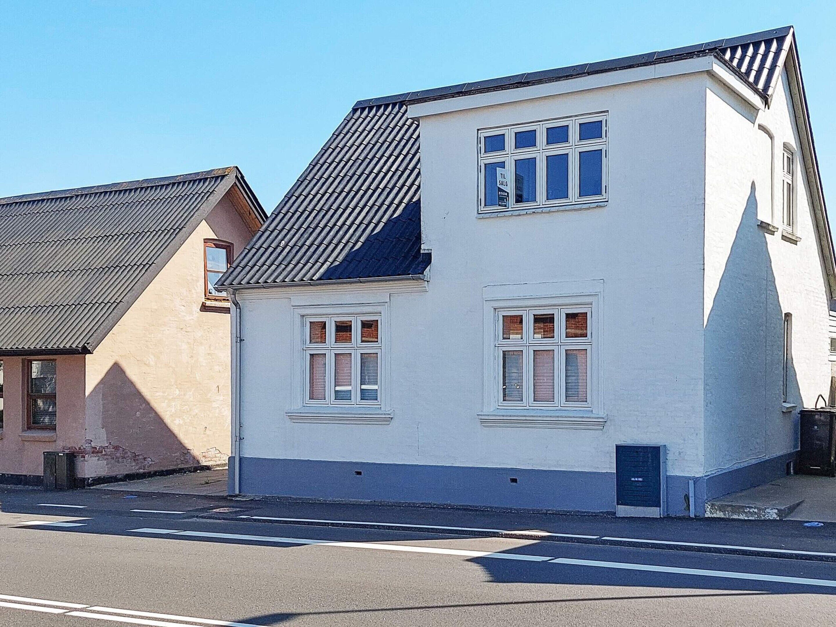 Une maison à deux étages, dotée d’un toit en pente, de murs extérieurs blancs et de nombreuses fenêtres.