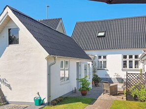 A white house with a dark roof, a visible window, and a small garden area with a potted plant and a green watering can. - 6 Person Holiday Home in Frederikshavn-by Traum (Frederikshavn)