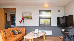 A modern living room with a leather sofa, a wooden coffee table, a TV, and a window with a view of greenery. - 8 Person Holiday Home in Romo (Rømø)