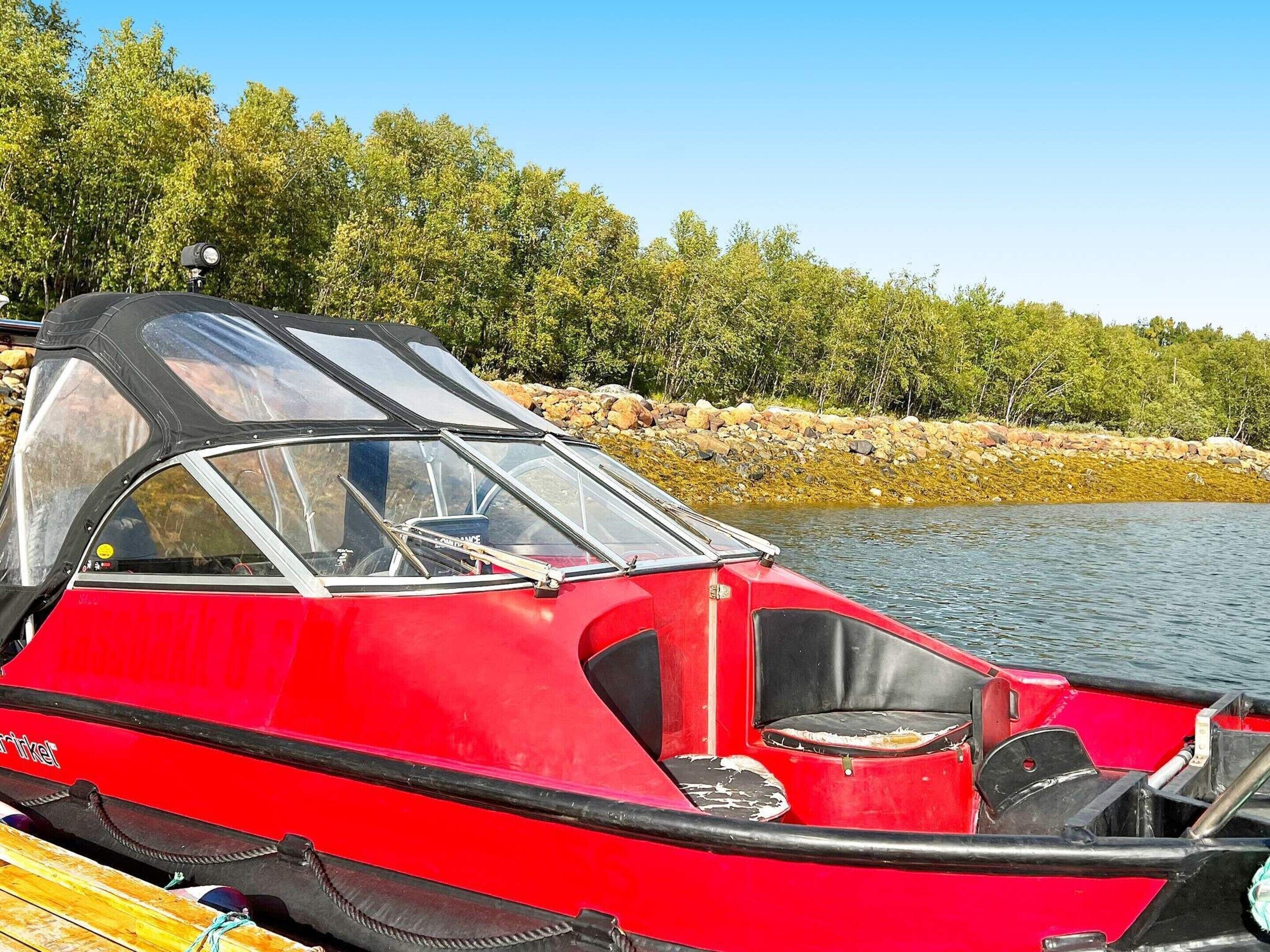 A red boat with a black canopy, docked at a lake with trees in the background.