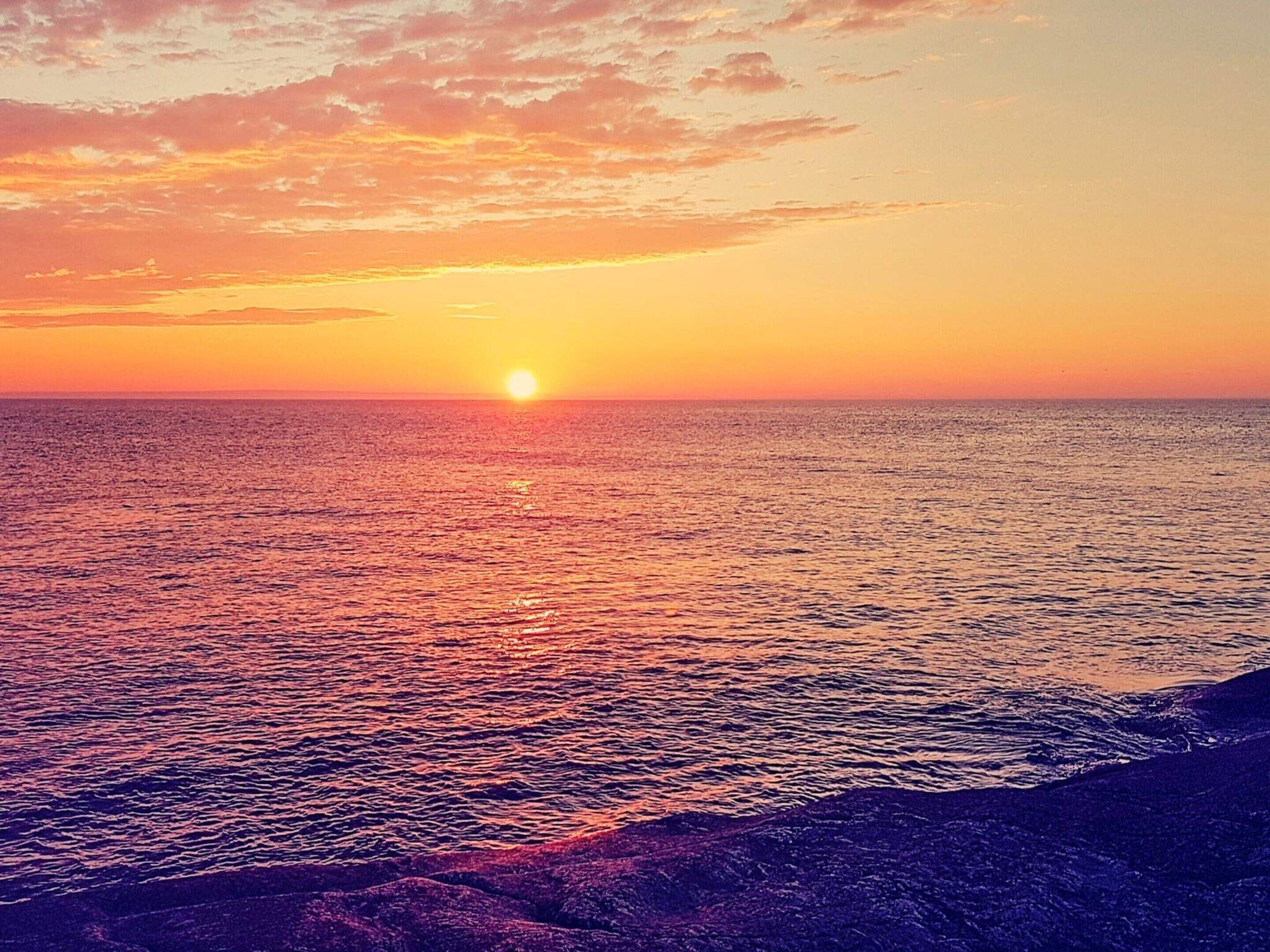 A sunset over a calm sea with a rocky shoreline.