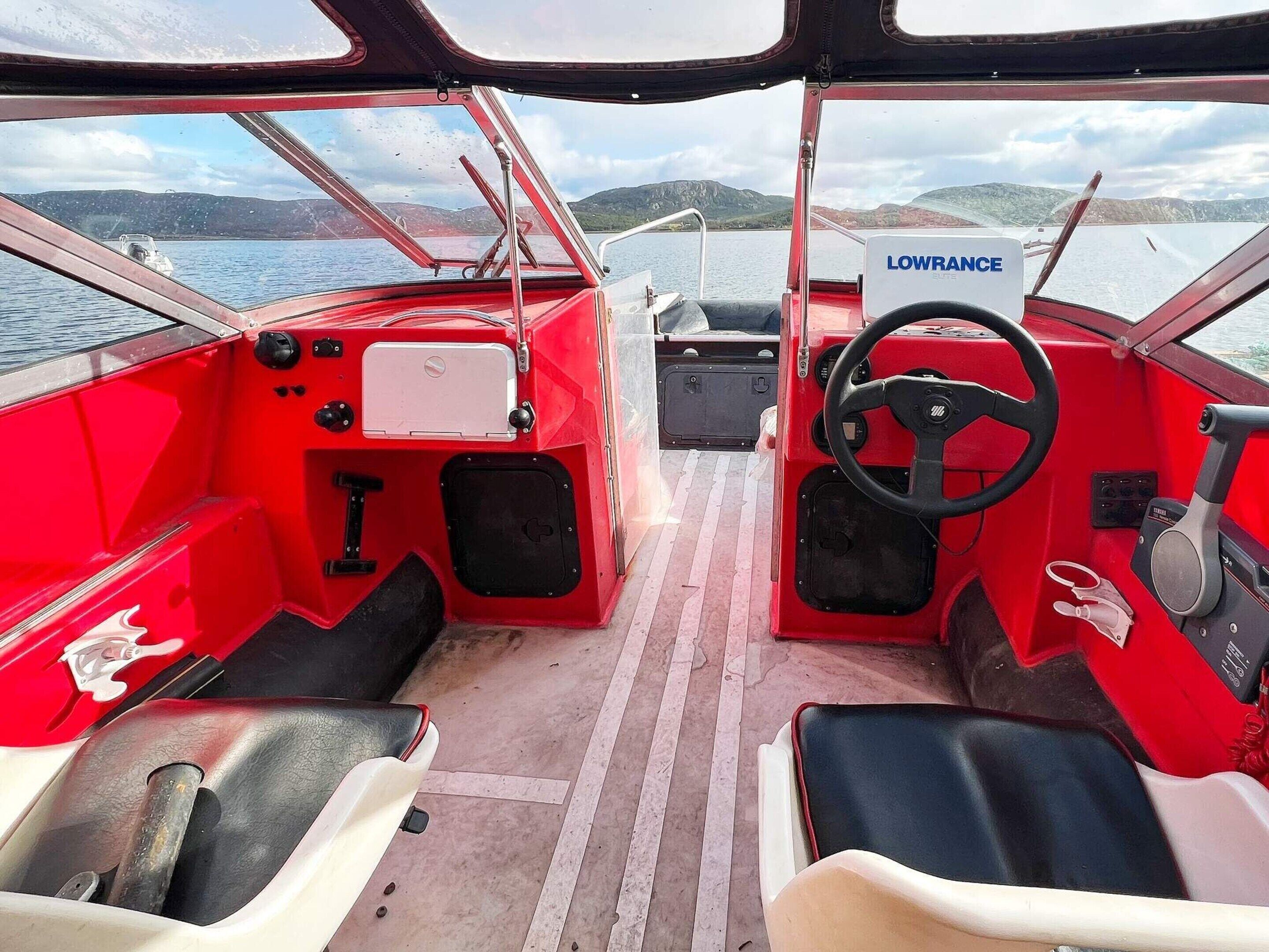 The interior of a red boat with a steering wheel, a control panel, and a sign reading "LOWRANCE."