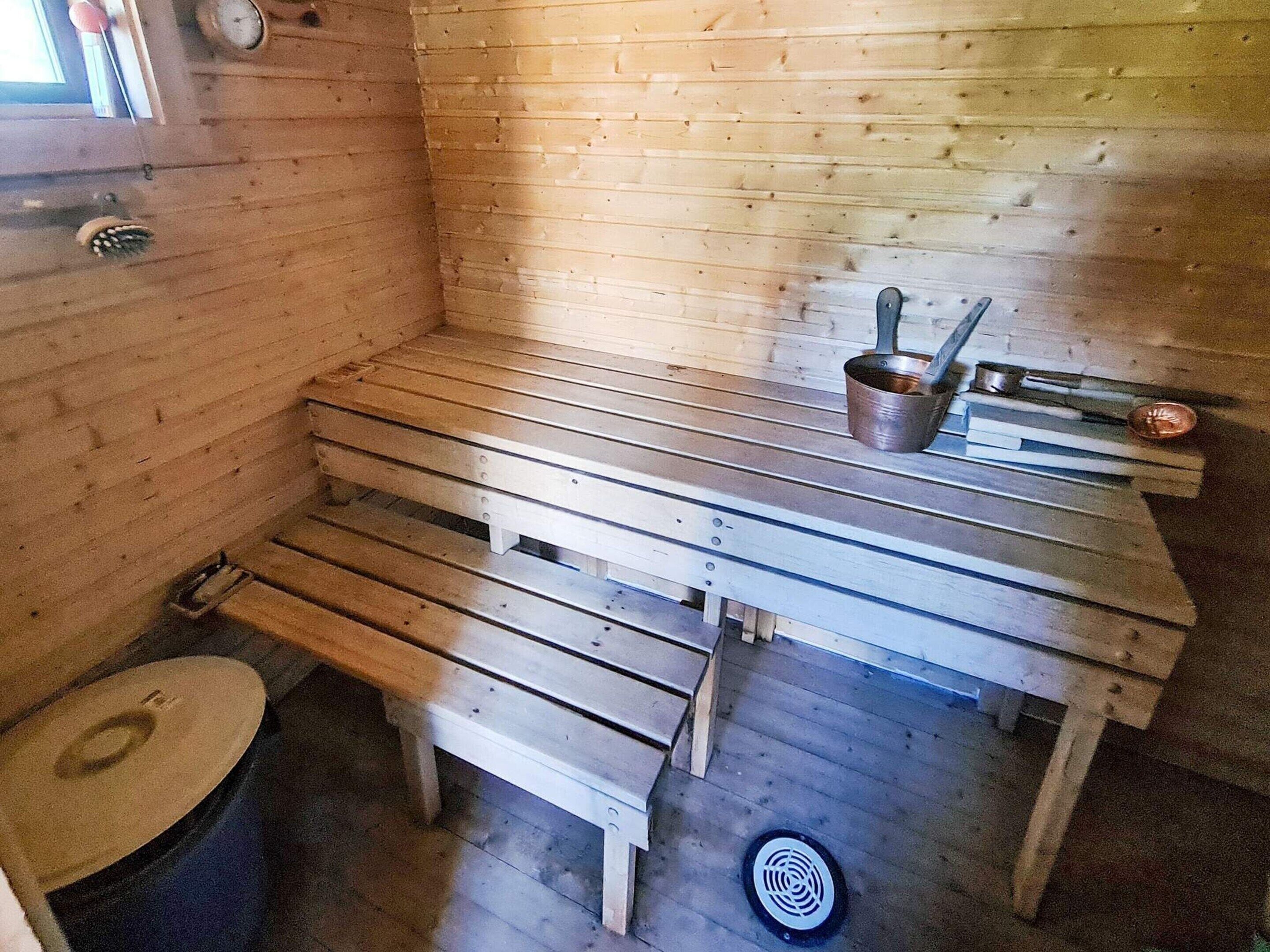 A sauna room with benches, a bucket, and a metal container.