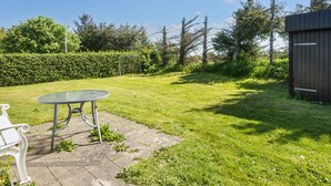 A grassy backyard with a metal table and bench, a wooden shed, and a hedge. - 6 Person Holiday Home in Tarm (Tarm)