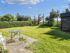 A grassy backyard with a metal table and bench, a wooden shed, and a hedge.