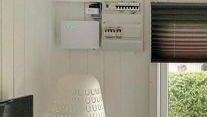 En servicepanel med elektriska komponenter, en termostat och ett fönster med persienner.