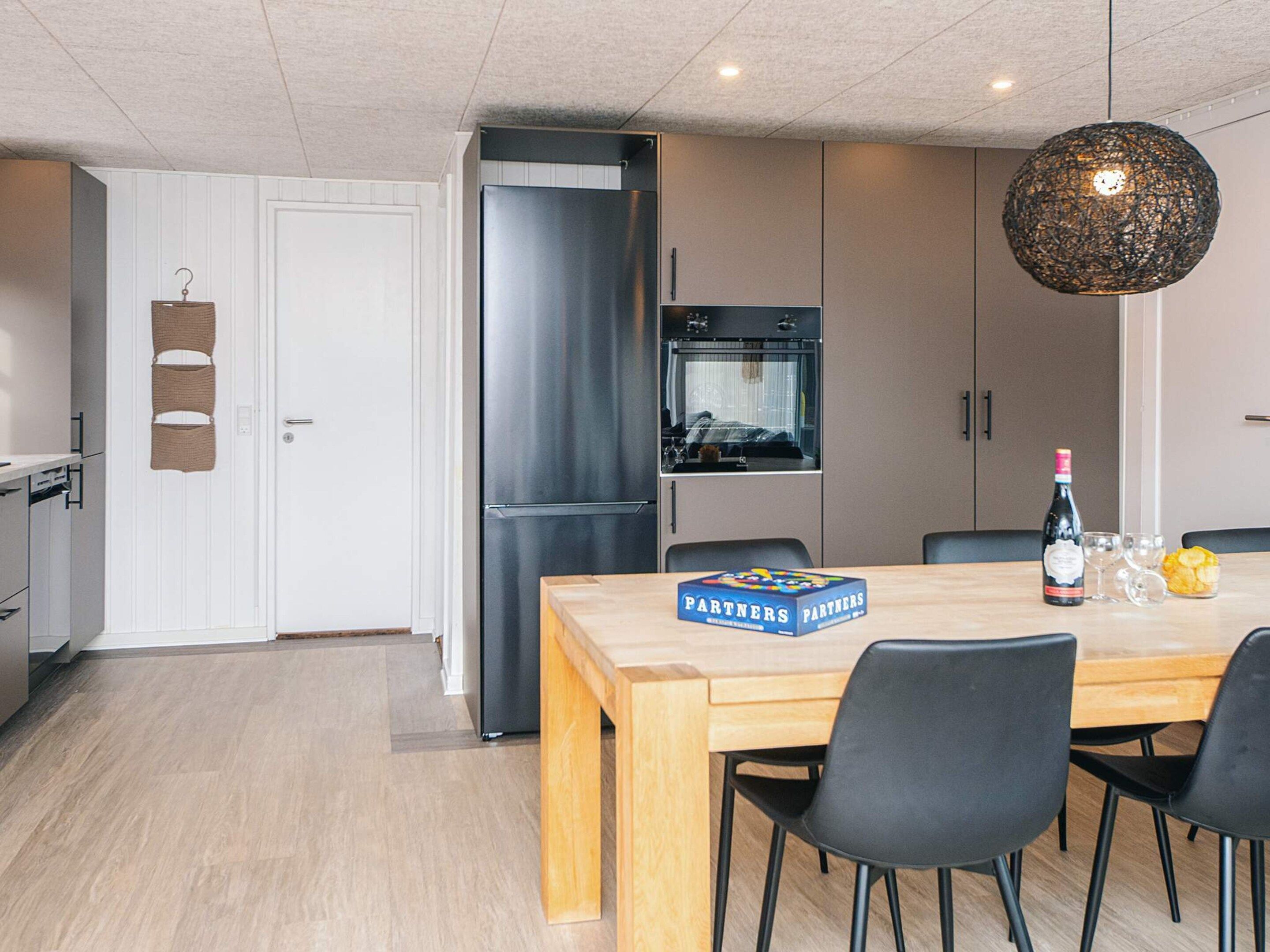 A modern kitchen with a stainless steel refrigerator, a wooden dining table with chairs, and a hanging light fixture.