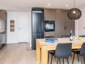 A modern kitchen with a stainless steel refrigerator, a wooden dining table with chairs, and a hanging light fixture. - 6 Person Holiday Home in Tarm (Tarm)