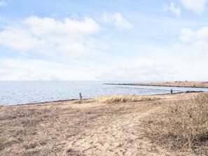 A coastal landscape with a sandy beach, a calm sea, and a clear sky.