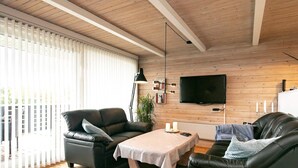 A modern living room with a wooden ceiling, a black leather sofa, a small round table, and a TV mounted on the wall. - 6 Person Holiday Home in Hals (Hals)
