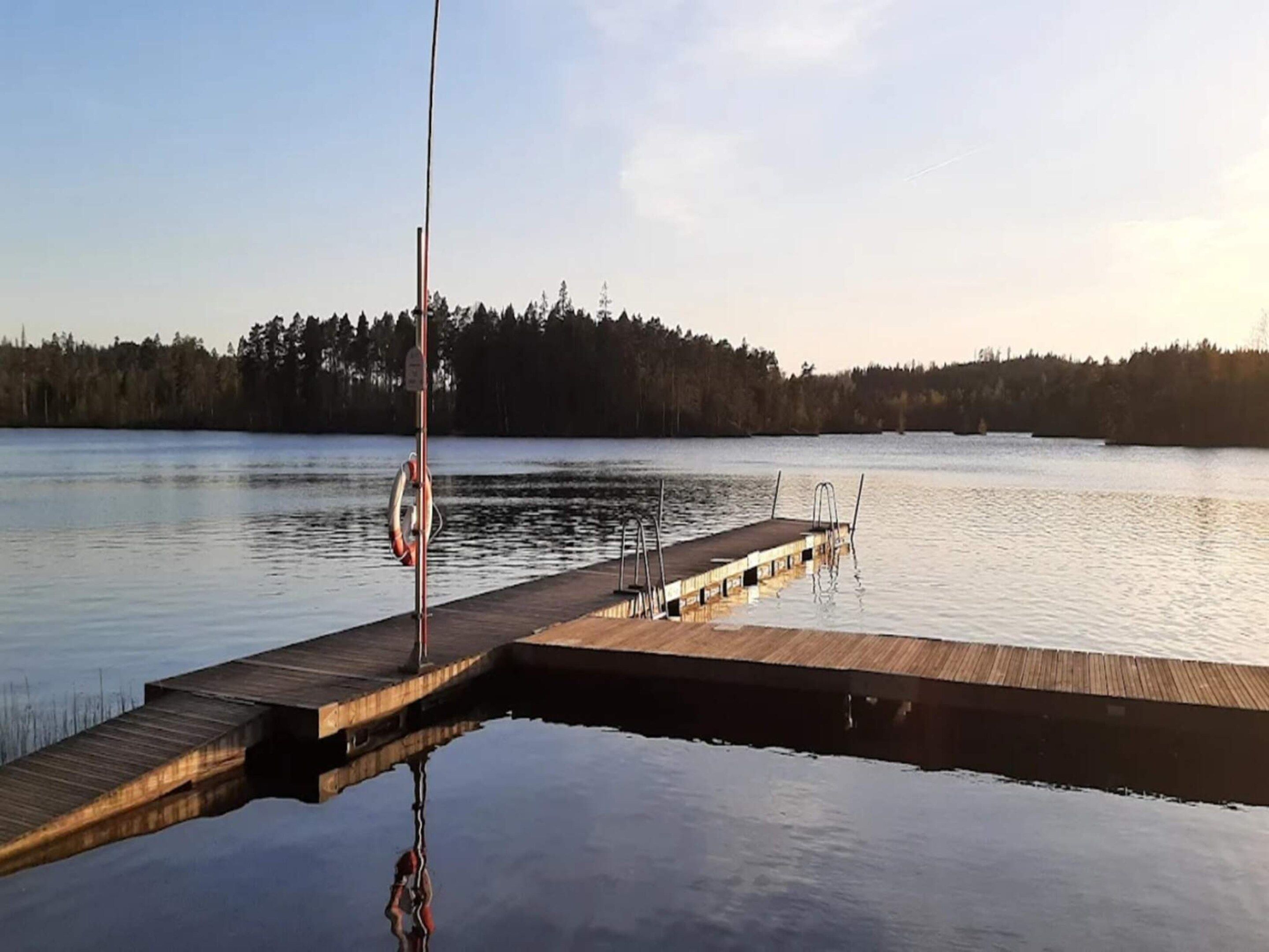 Un lac paisible, avec une jetée en bois qui s’avance sur l’eau, entouré d’arbres.