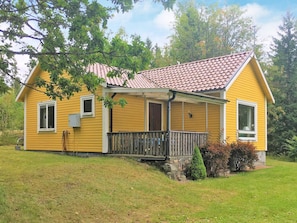 A yellow house with a red-tiled roof, a wooden porch, and a small front yard.