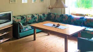 Una sala de estar con una mesa de madera, un sofá con tapicería floral, un televisor y una lámpara colgante.