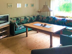 A living room with a wooden table, a sofa with floral upholstery, a television, and a hanging lamp. - 4 Person Holiday Home in Rorvik (Rörvik)