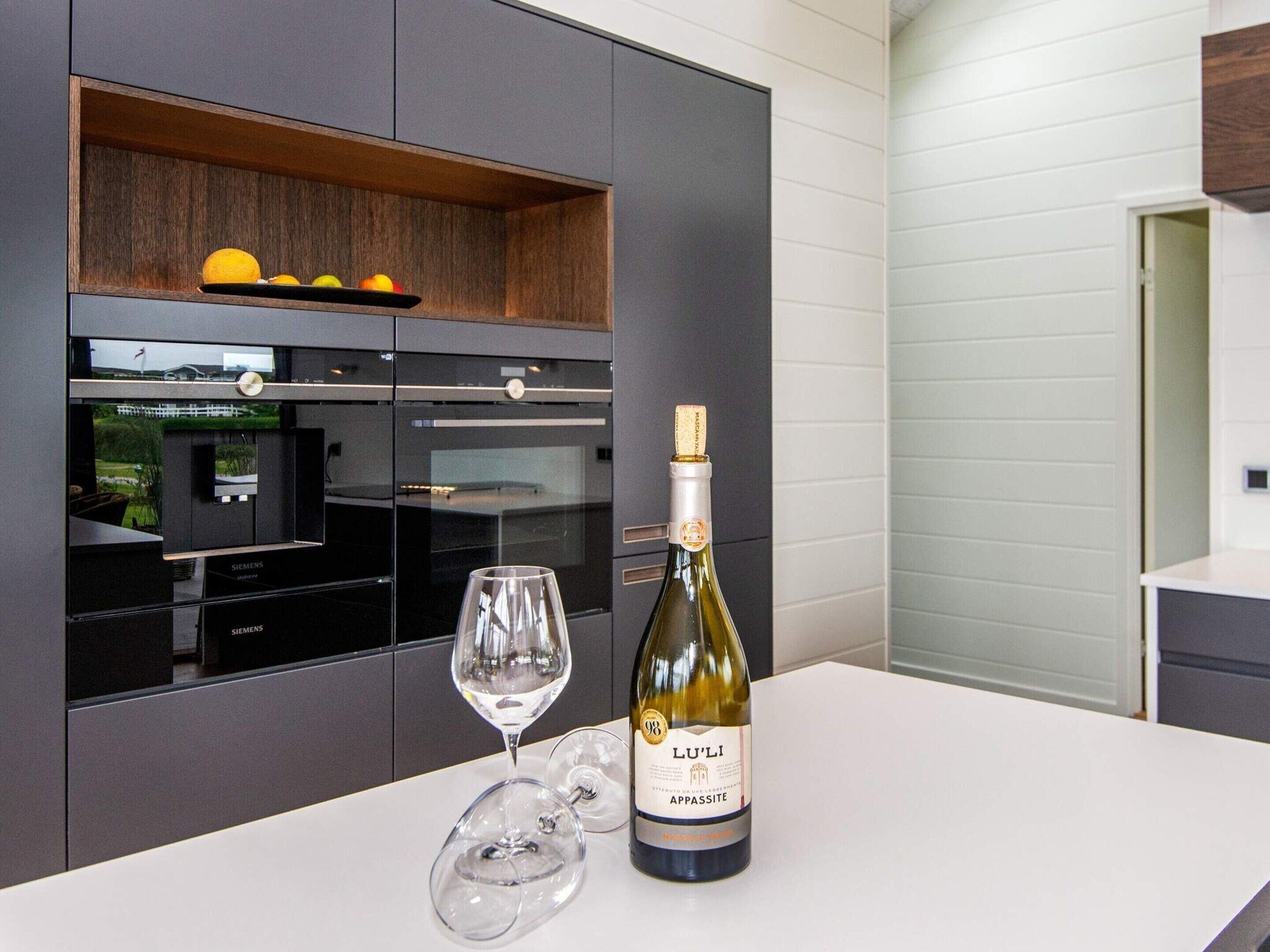 A modern kitchen with built-in appliances, a wine bottle, and two wine glasses on a white countertop.