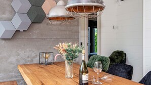 Una mesa de comedor de madera con una botella de vino y copas, un florero con plantas secas y una lámpara vintage.