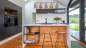 Una cocina moderna con una isla central, taburetes de bar, horno empotrado y un amplio ventanal con vistas al exterior.