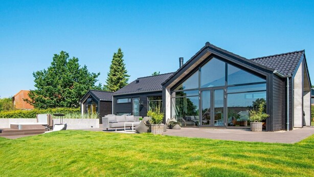 Una casa moderna con un amplio frente de cristal, un césped cuidado y mobiliario exterior.