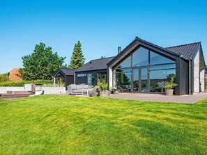 Una casa moderna con un amplio frente de cristal, un césped cuidado y mobiliario exterior.