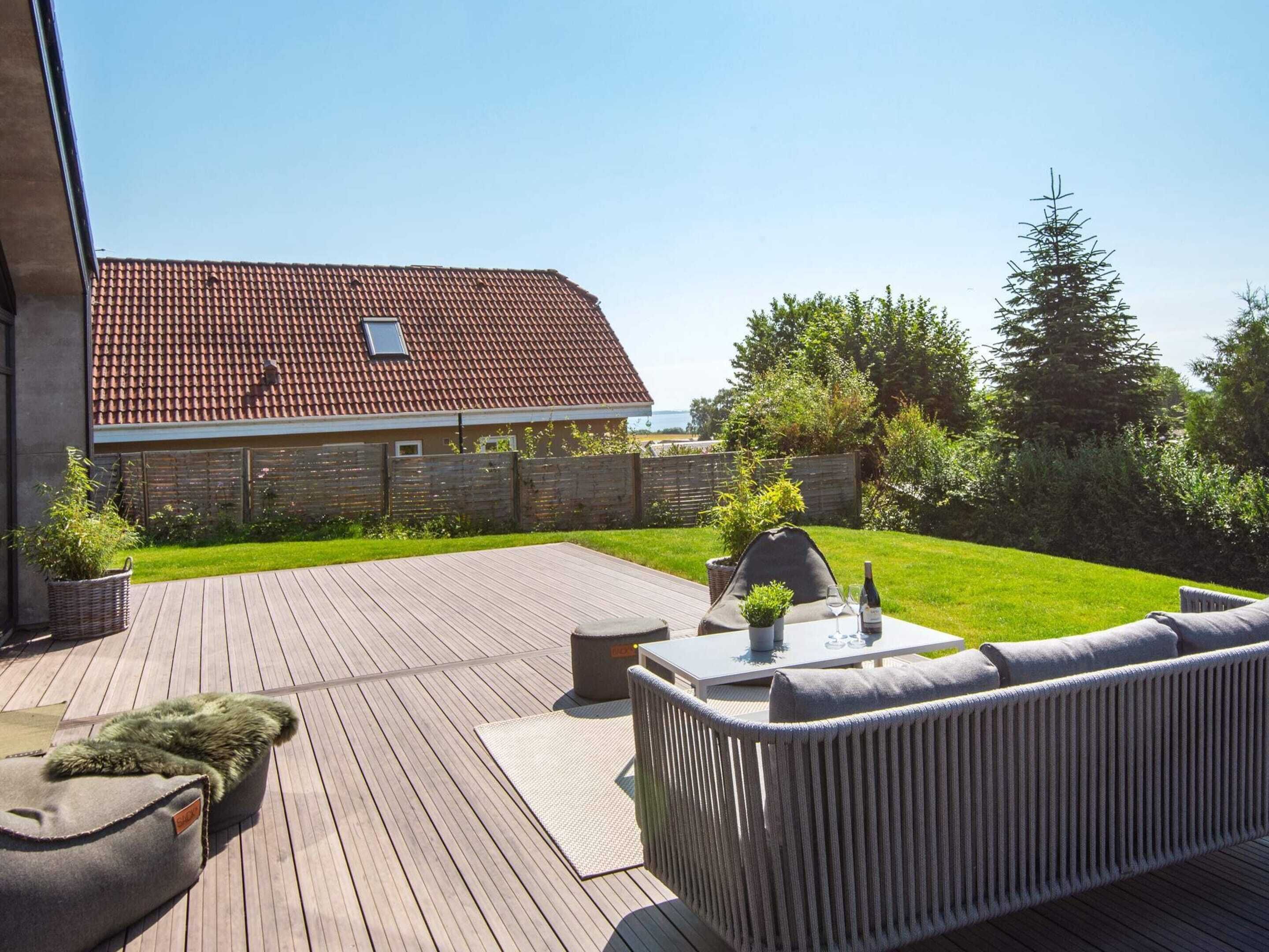 A wooden deck with a built-in sofa and a grill, surrounded by a well-maintained lawn and a wooden fence.