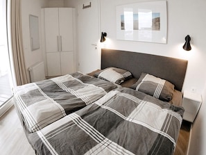 A double bed with a grey and white checkered bedspread, a grey headboard, and two bedside lamps. - 5 Star Holiday Home in Wendtorf (Wendtorf)