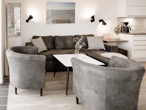 A modern living room with a grey sofa, two armchairs, a coffee table, and a view of the sea through a window.