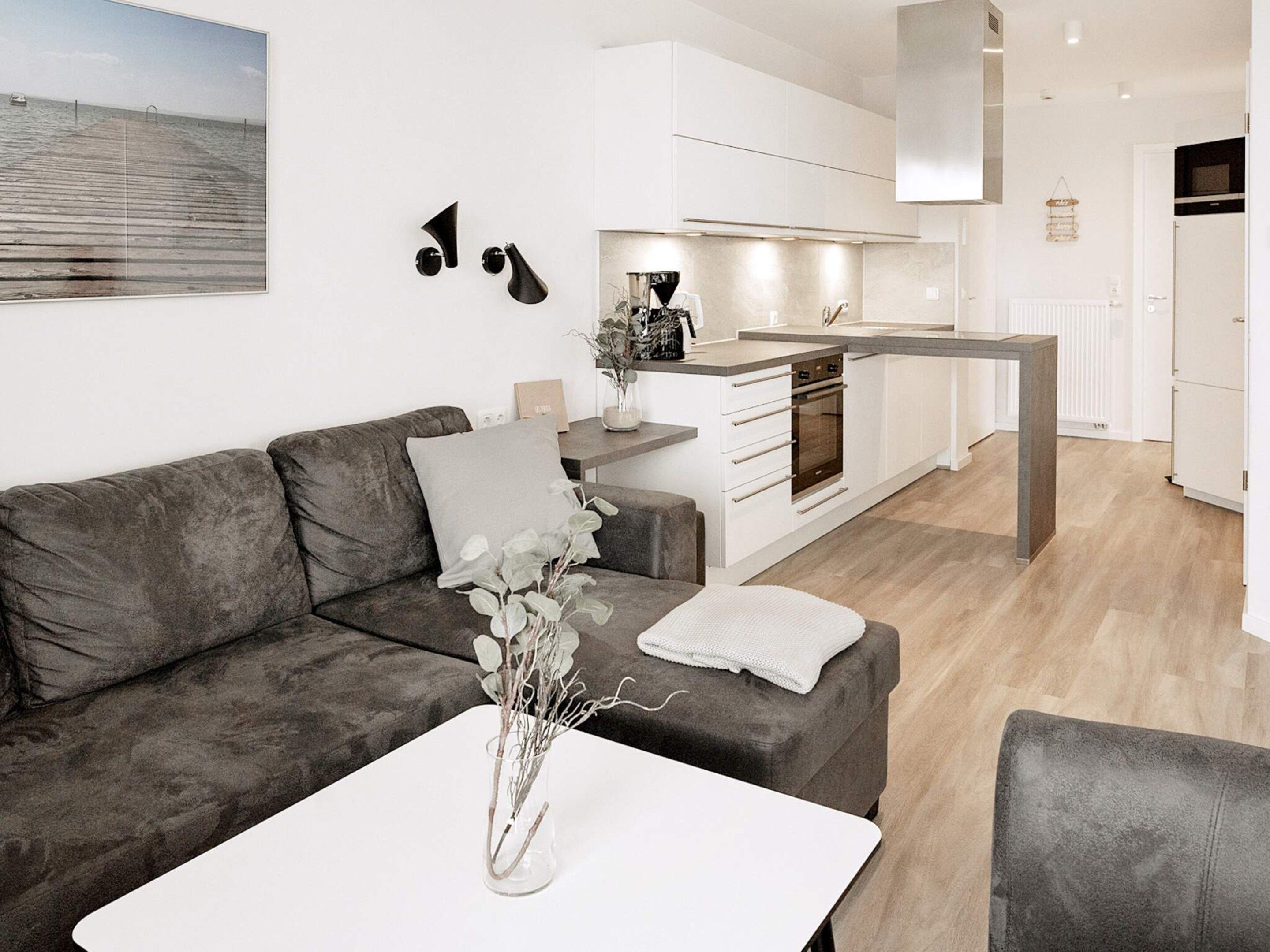 A modern living room with a grey sofa, a white coffee table, and a vase with branches.