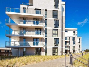 Un immeuble résidentiel à plusieurs étages, doté de balcons, de grandes fenêtres et surplombant un ciel dégagé.