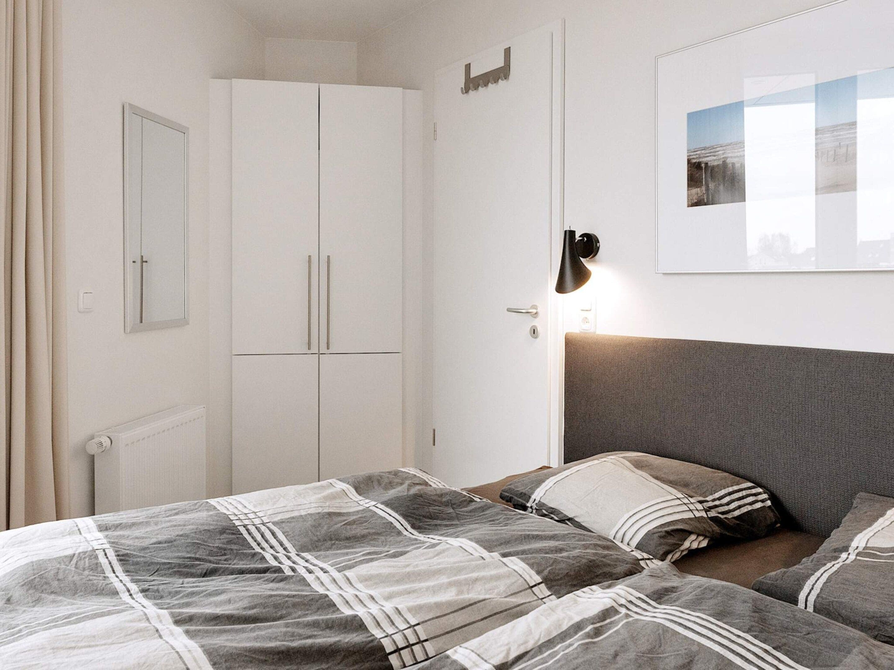 A bedroom with a bed, a wardrobe, a wall-mounted light, and a framed picture.