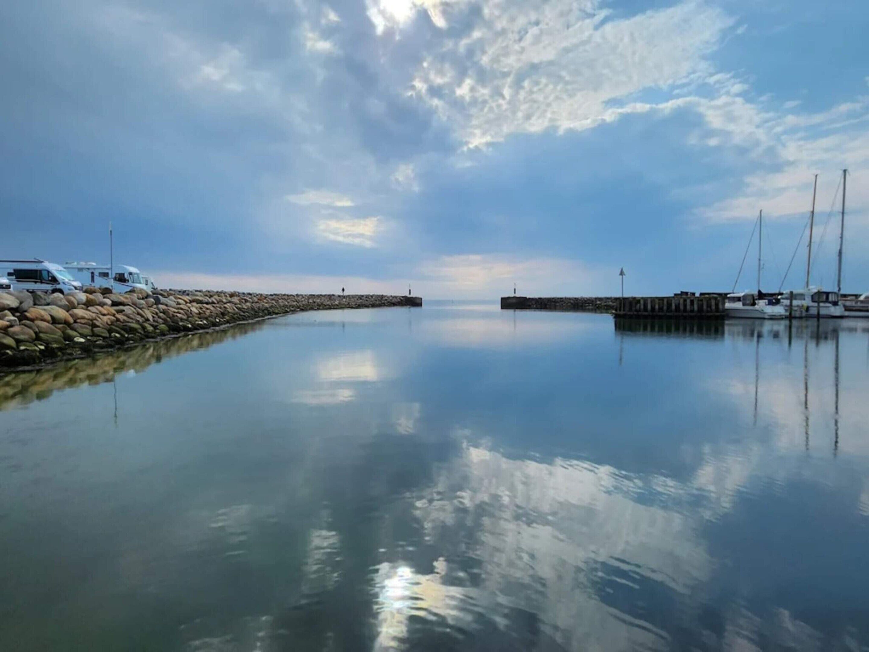 A calm waterfront with a row of boats docked, a stone breakwater, and a clear sky.